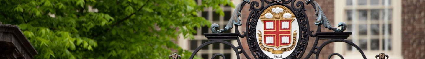 close up of the top of an outside gate showing Brown's logo with a brick building behind it
